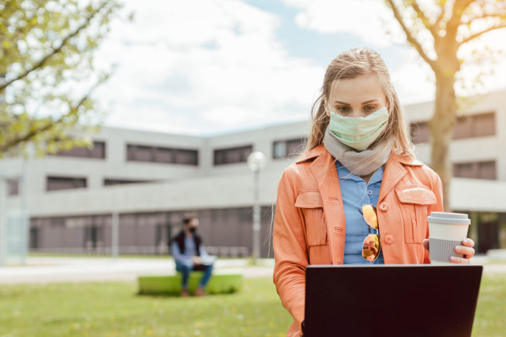 College student sitting outside on campus in mask
