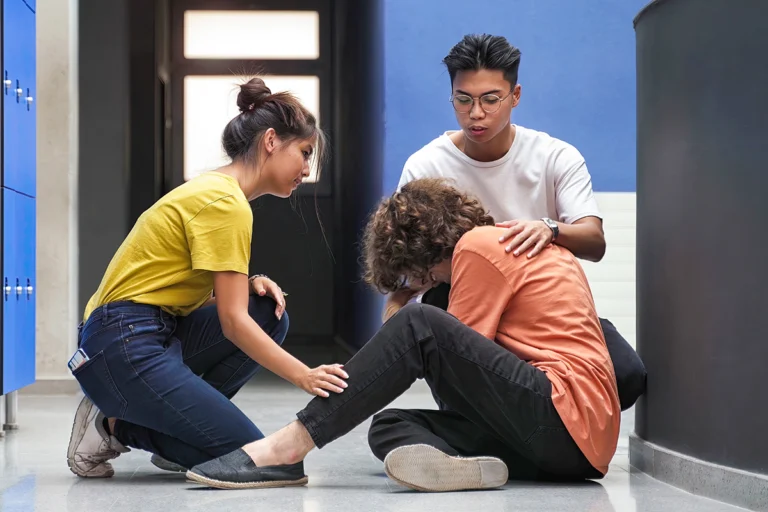 Two students comforting their classmate sitting on the floor in college hallway.